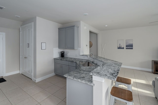 kitchen with gray cabinets, sink, a breakfast bar area, light tile patterned floors, and kitchen peninsula