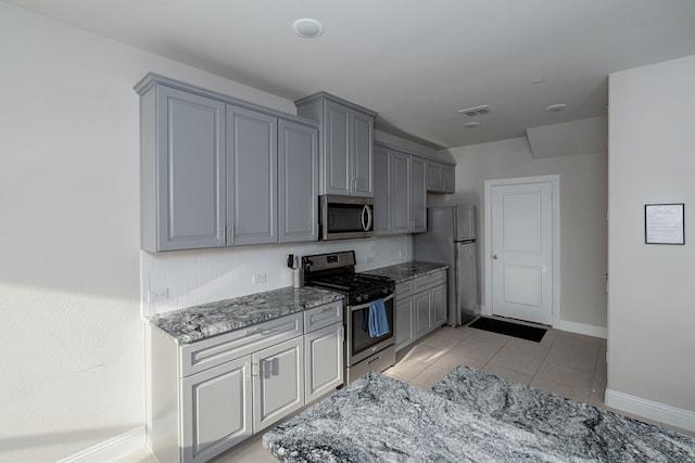 kitchen with gray cabinetry, light tile patterned floors, stone countertops, and appliances with stainless steel finishes