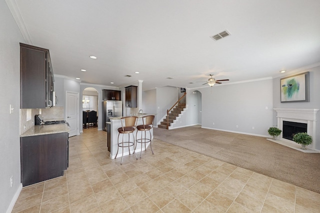 kitchen featuring ornamental molding, dark brown cabinets, stainless steel appliances, ceiling fan, and a breakfast bar area