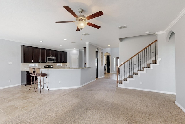 kitchen featuring a kitchen breakfast bar, crown molding, light tile patterned floors, appliances with stainless steel finishes, and dark brown cabinets