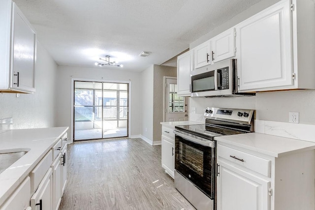 kitchen with appliances with stainless steel finishes, white cabinets, and light hardwood / wood-style flooring