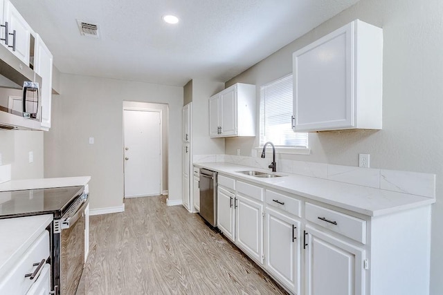 kitchen with stainless steel appliances, white cabinetry, sink, and light hardwood / wood-style floors