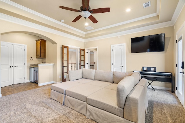 living room with a tray ceiling, ceiling fan, light colored carpet, and ornamental molding