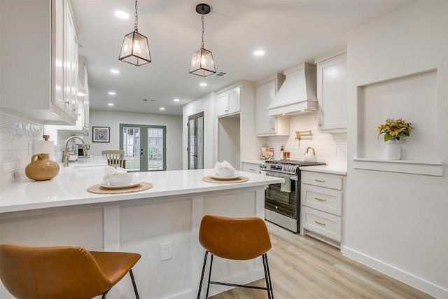 kitchen featuring kitchen peninsula, premium range hood, a breakfast bar, stainless steel range oven, and white cabinets