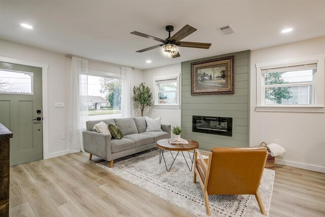 living room with ceiling fan, a large fireplace, and light hardwood / wood-style flooring