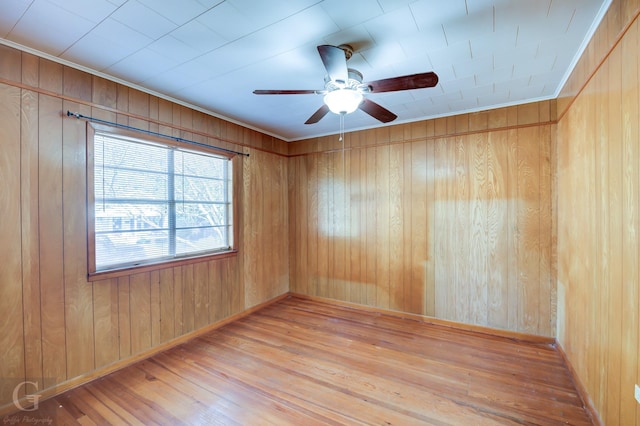 spare room with ceiling fan, wood walls, ornamental molding, and light wood-type flooring