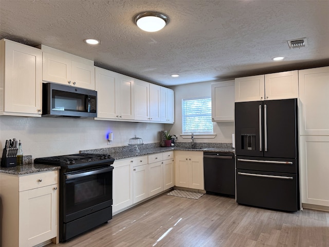 kitchen featuring light hardwood / wood-style flooring, white cabinetry, dark stone countertops, and black appliances