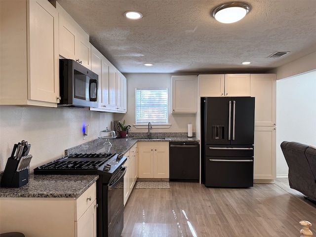 kitchen featuring sink, dark stone counters, white cabinets, black appliances, and light wood-type flooring