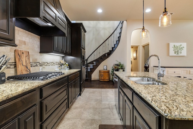 kitchen featuring a kitchen island with sink, a sink, decorative backsplash, appliances with stainless steel finishes, and pendant lighting