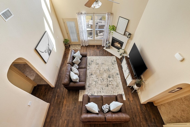 living room with dark hardwood / wood-style flooring, a towering ceiling, and ceiling fan