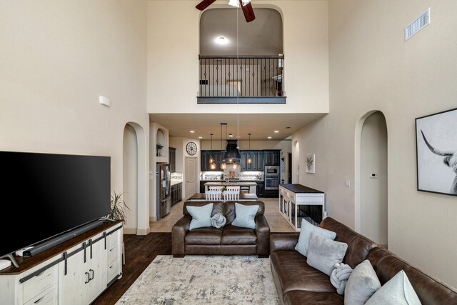 living room with ceiling fan, a towering ceiling, and dark wood-type flooring