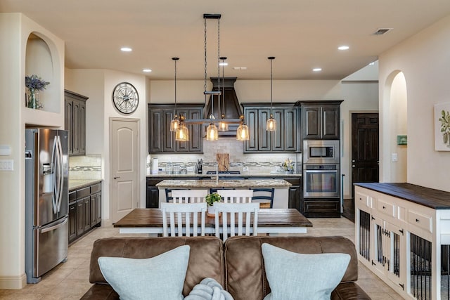 kitchen featuring pendant lighting, stainless steel appliances, tasteful backsplash, and a center island with sink