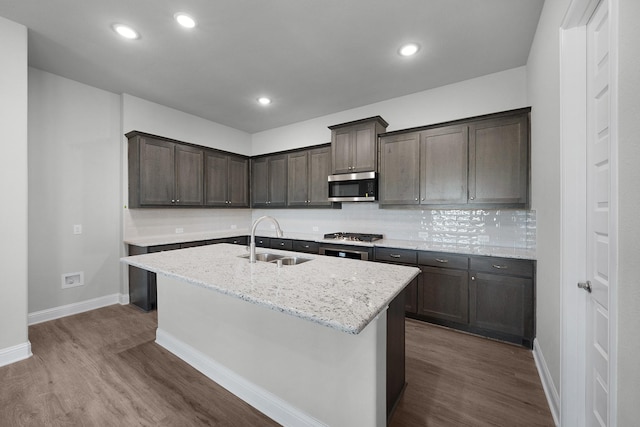 kitchen featuring a kitchen island with sink, sink, light stone countertops, and dark hardwood / wood-style floors