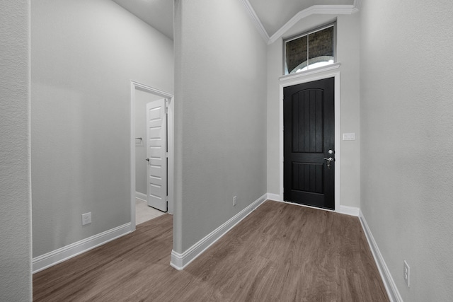 entryway with wood-type flooring, ornamental molding, and vaulted ceiling