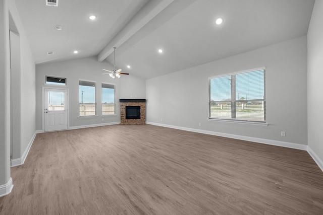 unfurnished living room with lofted ceiling with beams, ceiling fan, a stone fireplace, and a wealth of natural light