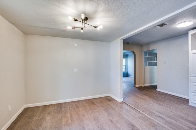 empty room with a chandelier, wood-type flooring, and a textured ceiling