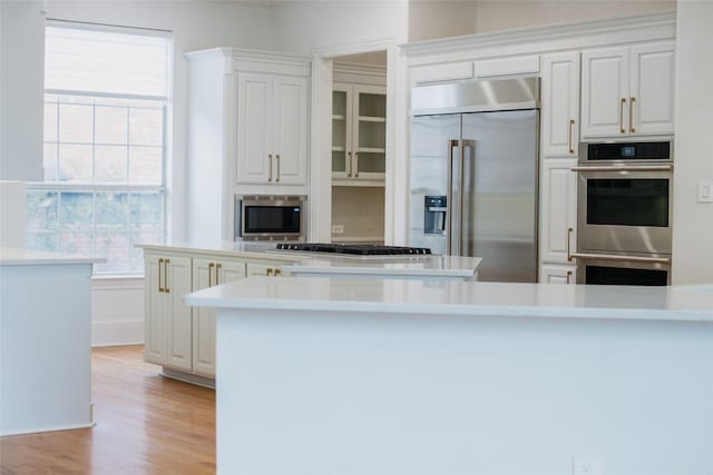 kitchen with built in appliances, white cabinetry, a center island, and light wood-type flooring