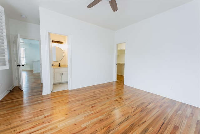 unfurnished bedroom featuring a walk in closet, light wood-type flooring, ensuite bathroom, ceiling fan, and sink