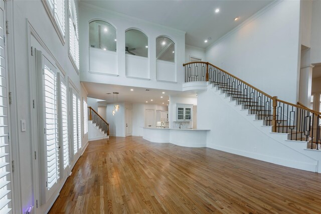 unfurnished living room featuring a towering ceiling, wood-type flooring, and ornamental molding