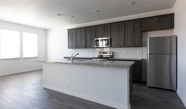 kitchen featuring sink, stainless steel appliances, light stone counters, dark hardwood / wood-style flooring, and a center island with sink