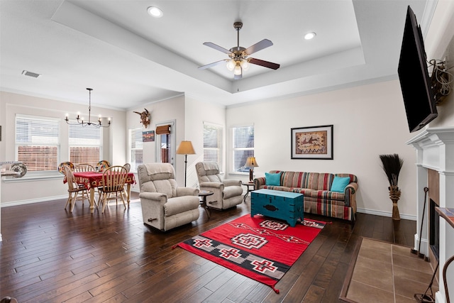 living room featuring a tray ceiling, dark wood-type flooring, ceiling fan with notable chandelier, and ornamental molding