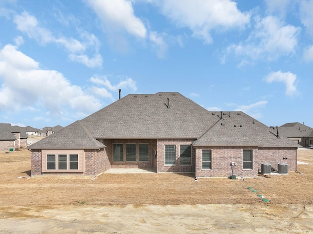 rear view of property with central AC unit, brick siding, and roof with shingles