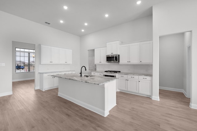 kitchen featuring visible vents, an island with sink, a sink, a towering ceiling, and stainless steel microwave