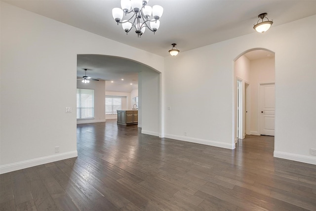 unfurnished room with ceiling fan with notable chandelier and dark wood-type flooring