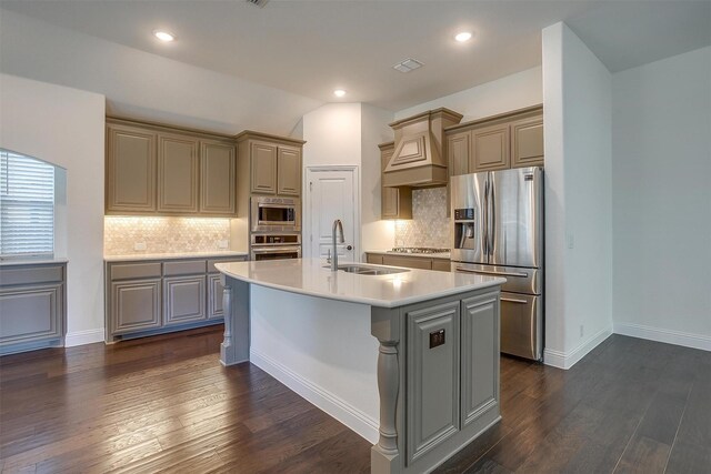 kitchen with sink, dark hardwood / wood-style floors, premium range hood, an island with sink, and appliances with stainless steel finishes