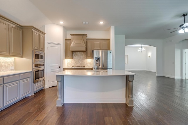 kitchen with appliances with stainless steel finishes, backsplash, dark hardwood / wood-style flooring, custom exhaust hood, and a kitchen island with sink