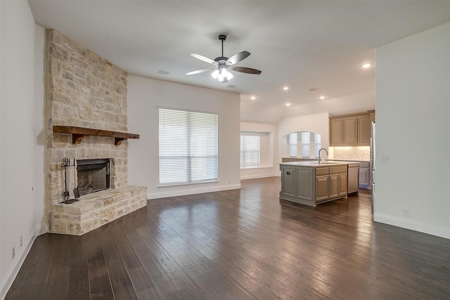 unfurnished living room featuring dark hardwood / wood-style floors, a stone fireplace, ceiling fan, and sink