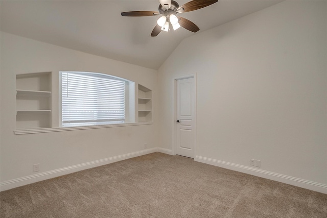 carpeted spare room featuring vaulted ceiling, built in features, and ceiling fan