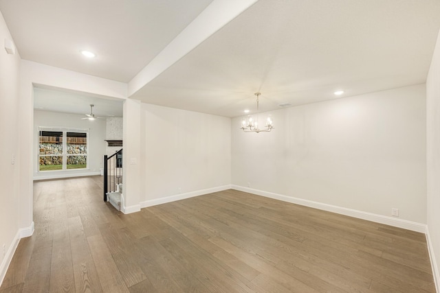 empty room with ceiling fan with notable chandelier and wood-type flooring