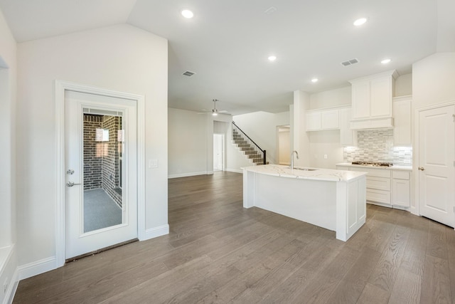 kitchen with light stone countertops, tasteful backsplash, vaulted ceiling, white cabinets, and an island with sink