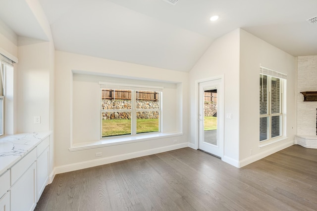 unfurnished dining area with hardwood / wood-style flooring, a stone fireplace, and lofted ceiling