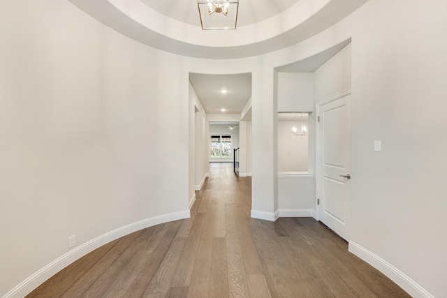 hallway featuring a chandelier, wood-type flooring, and a tray ceiling