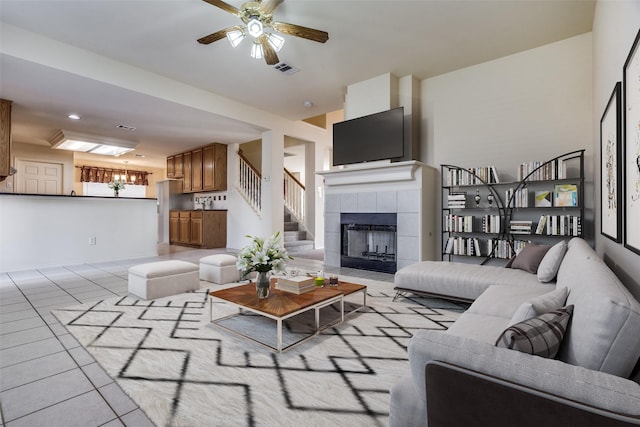 tiled living room with a fireplace and ceiling fan with notable chandelier