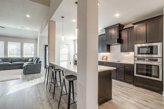 5214 Rowlan Row, Midlothian, TX 76065 - kitchen with stainless steel appliances, dark brown cabinetry, light wood-style floors, open floor plan, and light countertops