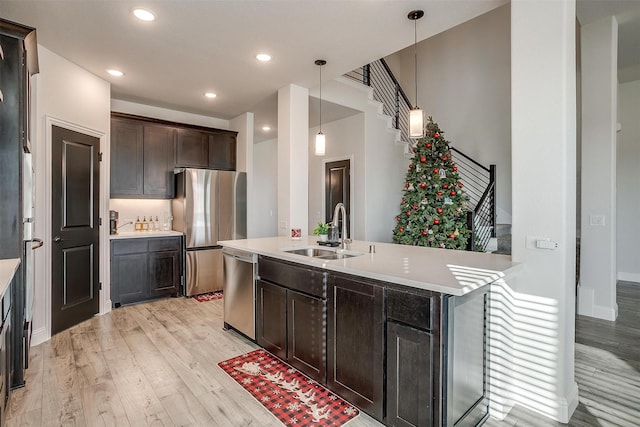 kitchen with a center island with sink, hanging light fixtures, sink, light wood-type flooring, and appliances with stainless steel finishes