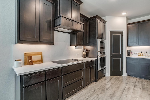 kitchen with dark brown cabinets, light wood-type flooring, stainless steel appliances, and custom range hood