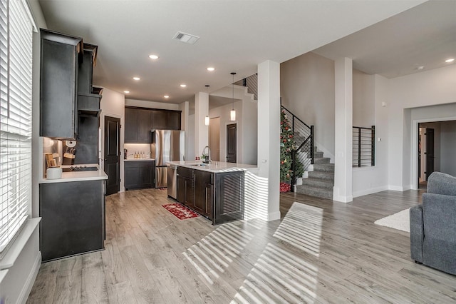 kitchen featuring stainless steel appliances, sink, light hardwood / wood-style floors, hanging light fixtures, and an island with sink