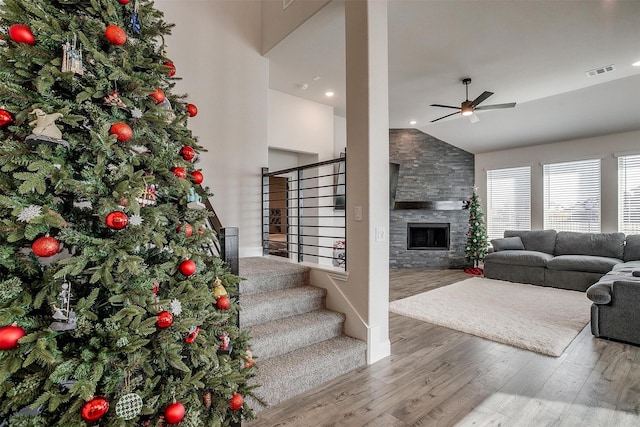 living room with ceiling fan, high vaulted ceiling, a stone fireplace, and hardwood / wood-style floors