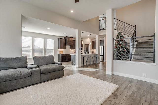 living room with sink, a towering ceiling, light hardwood / wood-style floors, and ceiling fan