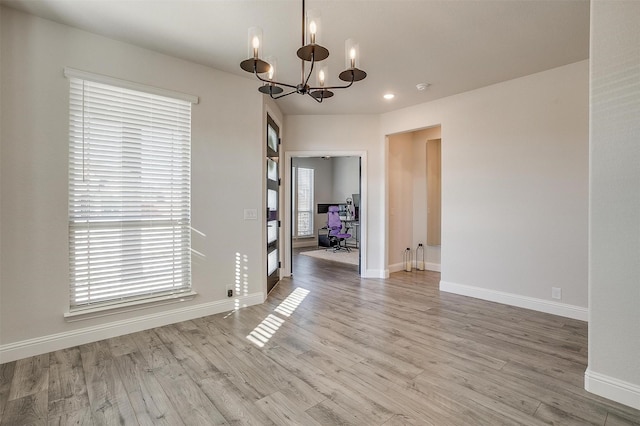 unfurnished room featuring a notable chandelier and light wood-type flooring