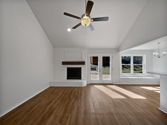 unfurnished living room with french doors, high vaulted ceiling, wood-type flooring, a fireplace, and ceiling fan with notable chandelier