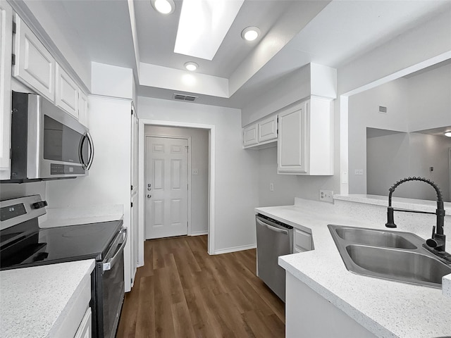 kitchen with a skylight, white cabinetry, sink, stainless steel appliances, and dark hardwood / wood-style floors