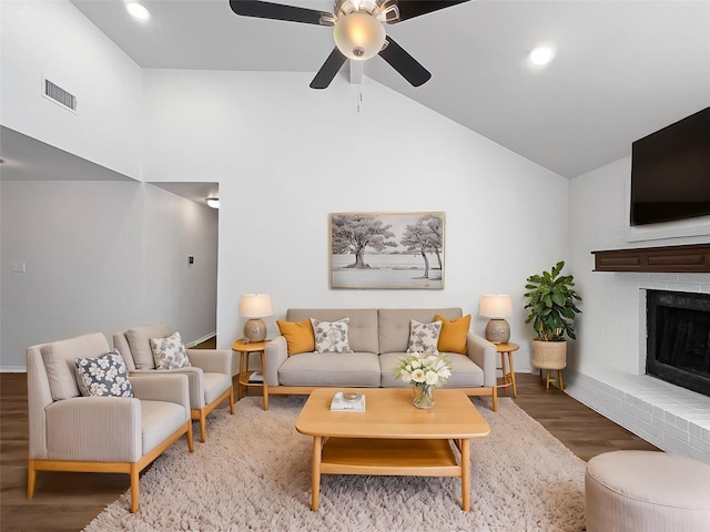 living room featuring hardwood / wood-style flooring, ceiling fan, high vaulted ceiling, and a brick fireplace