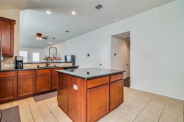 kitchen with a center island, dark stone counters, sink, ceiling fan, and decorative backsplash