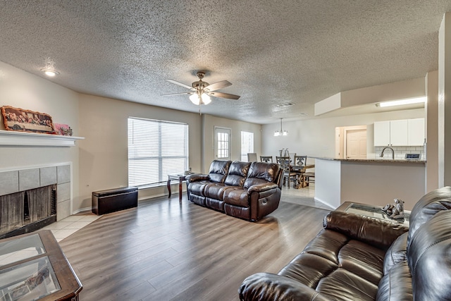 living room with a tiled fireplace, light hardwood / wood-style floors, and a textured ceiling