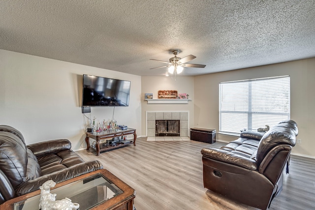 living room featuring ceiling fan, a fireplace, a textured ceiling, and hardwood / wood-style flooring